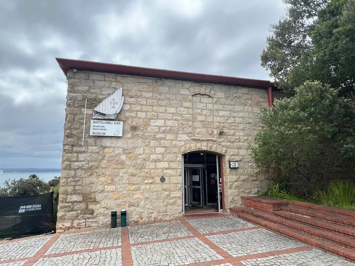 The stone-built Bartolomeu Dias Maritime Museum entrance with museum signage visible, cobbled forecourt leading up to the arched doorway