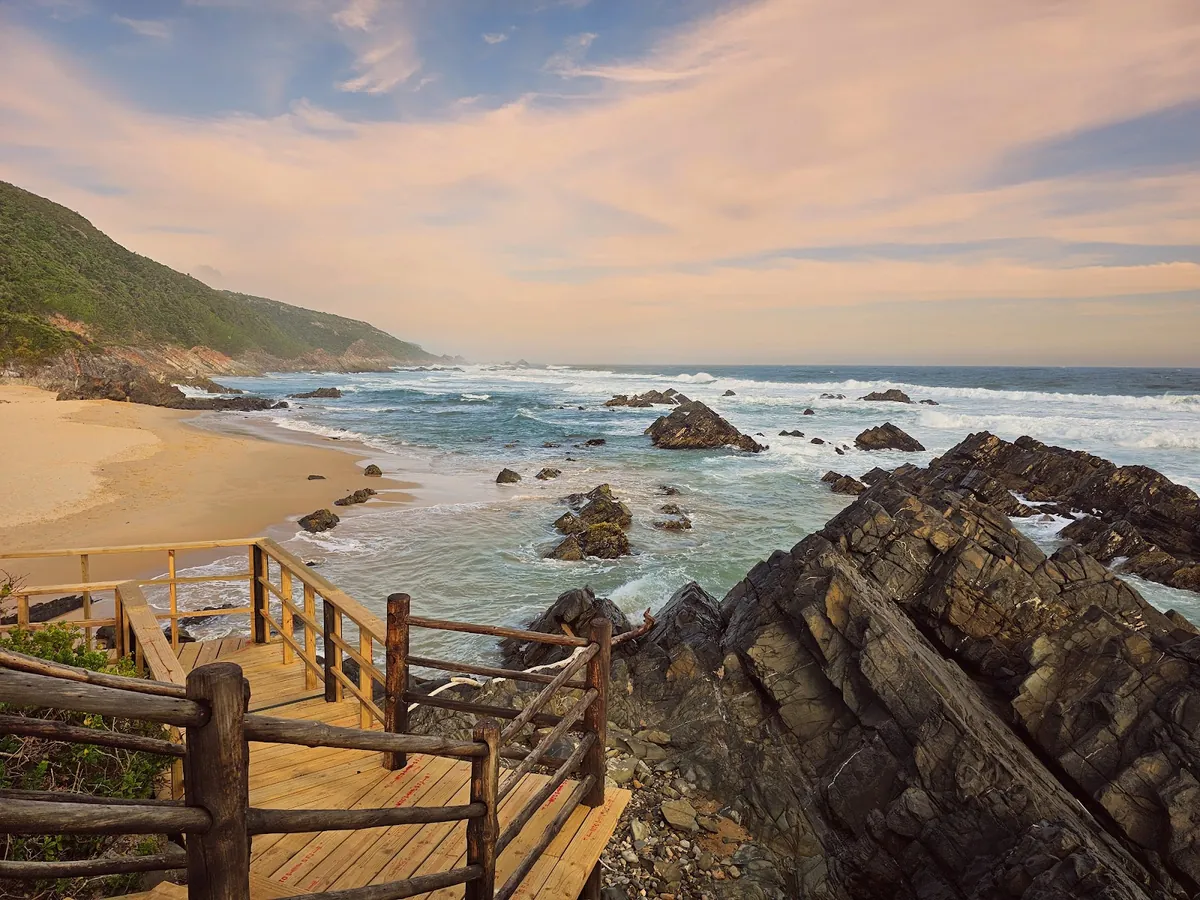 Keurboomstrand Beach east of Plettenberg Bay — broad empty sand, turquoise water, Tsitsikamma foothills beyond
