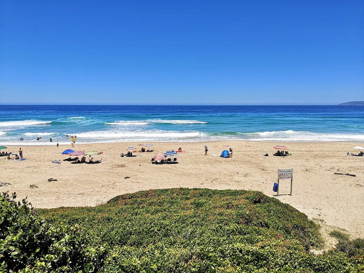 Empty stretch of golden sand at Keurboomstrand with footprints along the high-tide line and a vivid blue summer sky