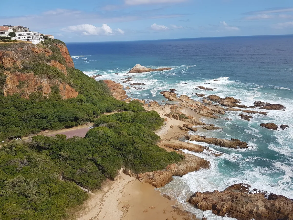 Knysna Heads from the Eastern Head viewpoint — rocky cliffs and lagoon mouth, Knysna homes visible across the water
