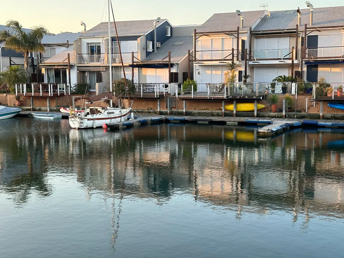 A sailing yacht moored at the Knysna Quays canal-edge homes at sunset, the water still and reflective