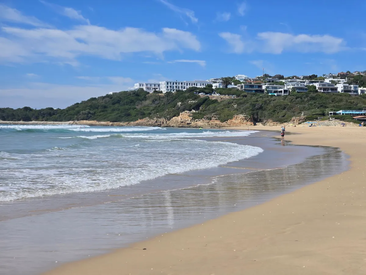 Lookout Beach shoreline curving toward the Beachy Head cliff, Plettenberg hotel complex visible on the hill above