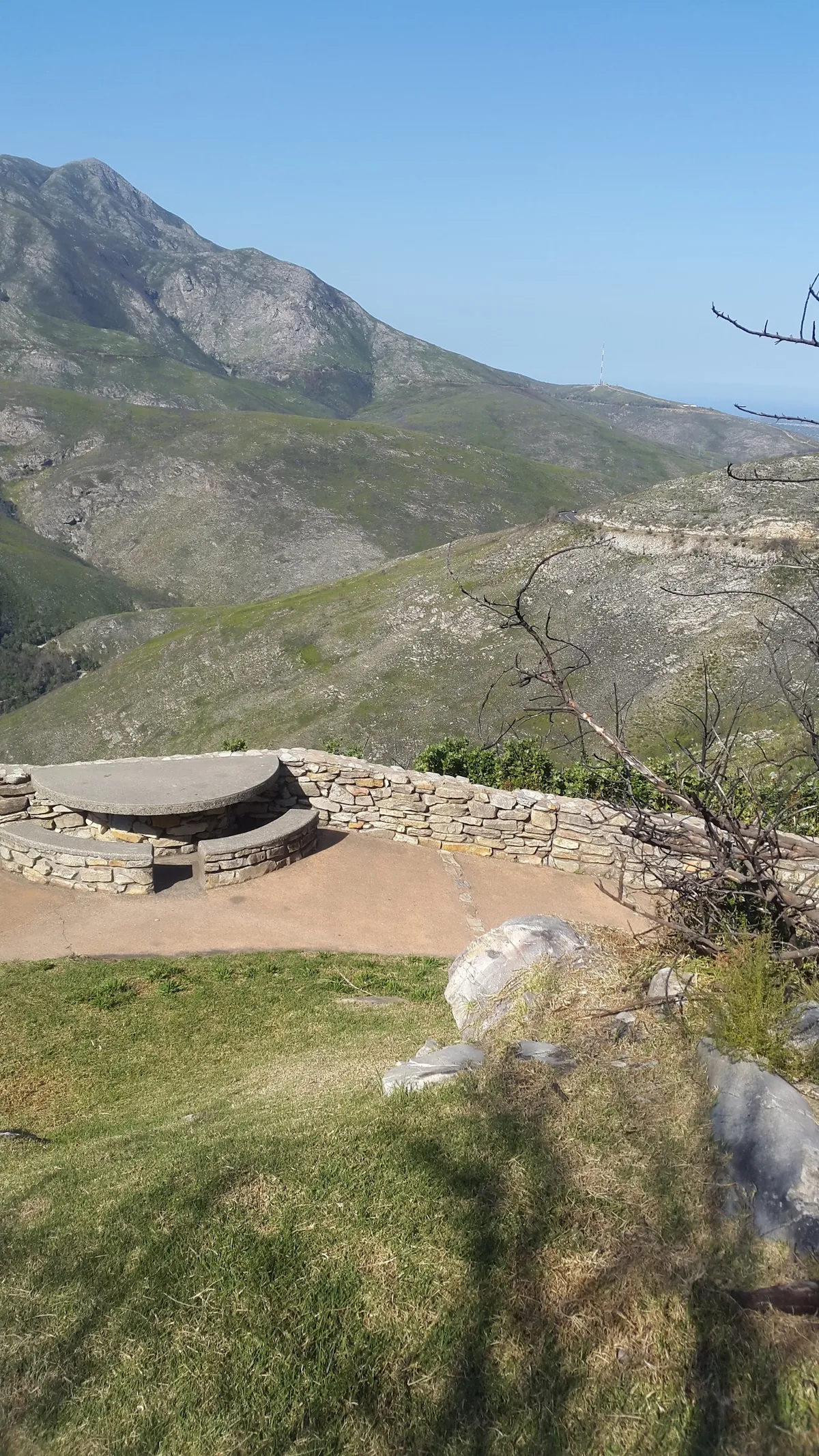 Round stone plinth at the Outeniqua Pass viewpoint with the bare inland flank of the mountain rising behind, low fynbos in the foreground