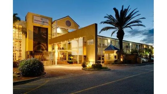 Protea Hotel by Marriott Knysna Quays entrance at dusk — palm tree, lit signage, low-rise hotel building