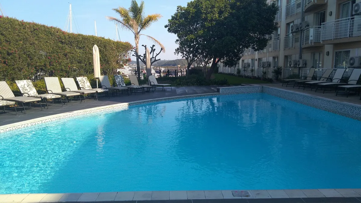 Protea Hotel Knysna Quays poolside deck — large pool, palm trees, marina masts visible behind the fence