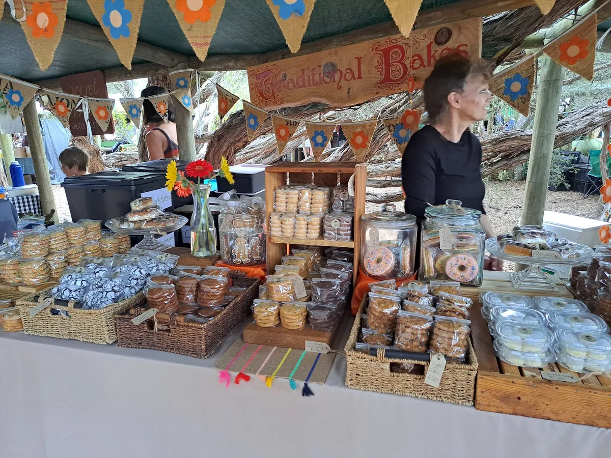 Wild Oats traditional bakes stall — jars of rusks, wooden crates of biscuits and cookies, bunting strung overhead, vendor behind the table