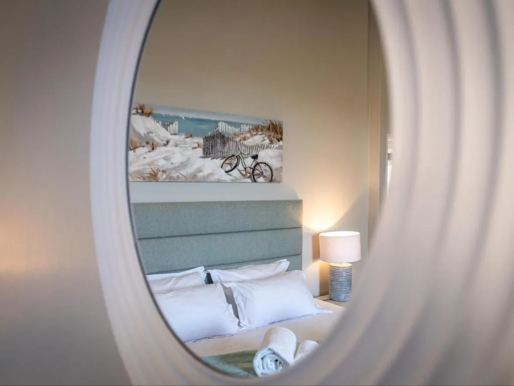 Modern bedroom with upholstered headboard, white pillows, bedside lamp, and coastal artwork