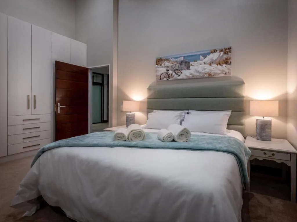 Modern bedroom with queen bed, gray headboard, rolled towels, and coastal artwork