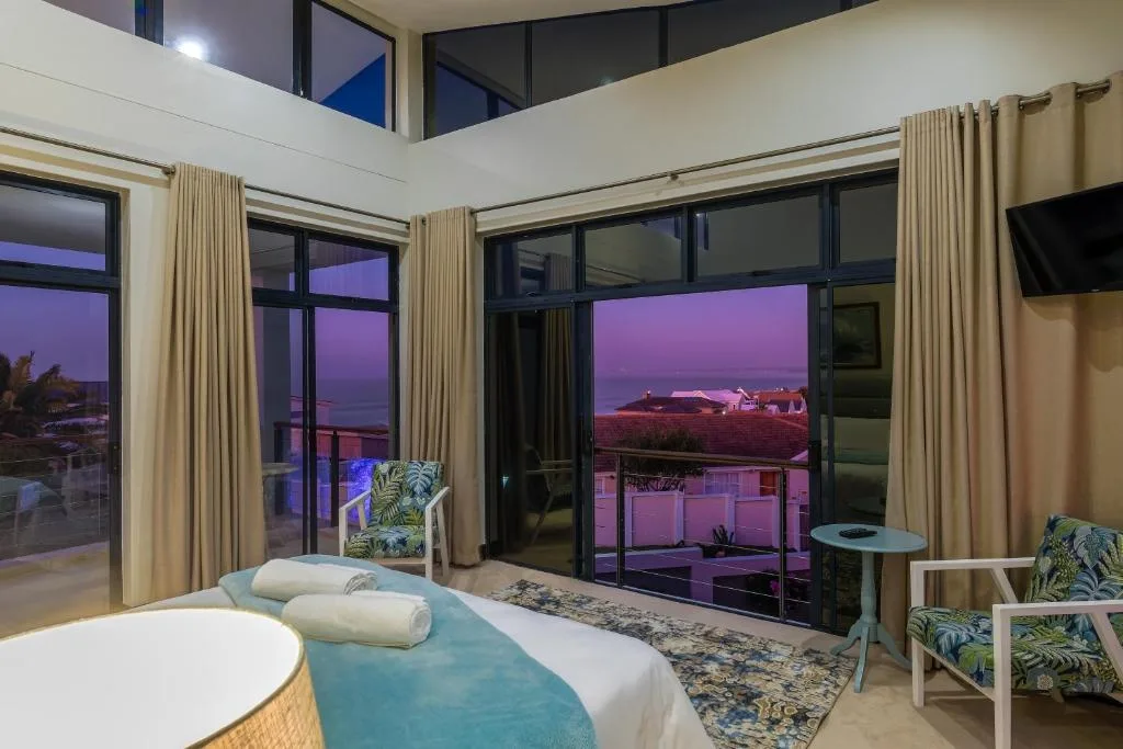 Modern bedroom with bed, ocean view through floor-to-ceiling windows at dusk