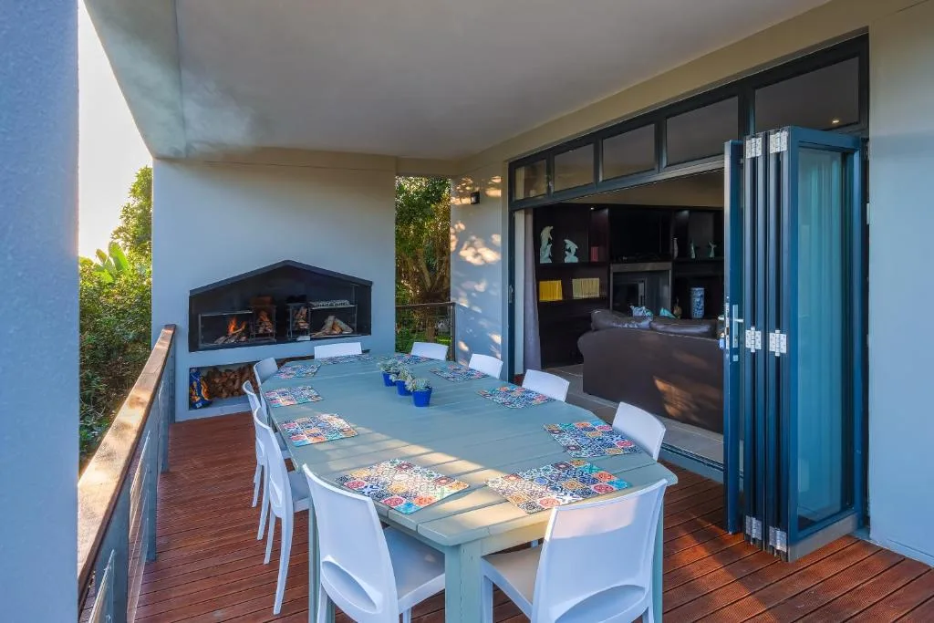 Outdoor covered deck with dining table, chairs, and built-in braai fireplace