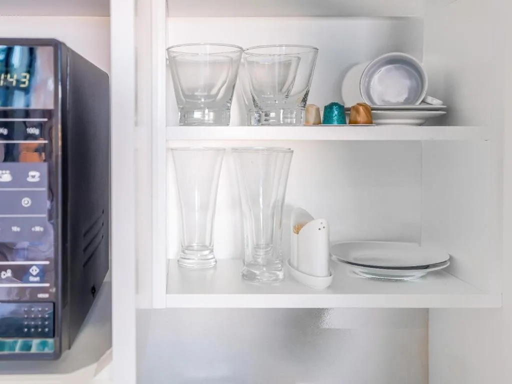 Open shelving displaying glassware, plates, and coffee capsules neatly organized