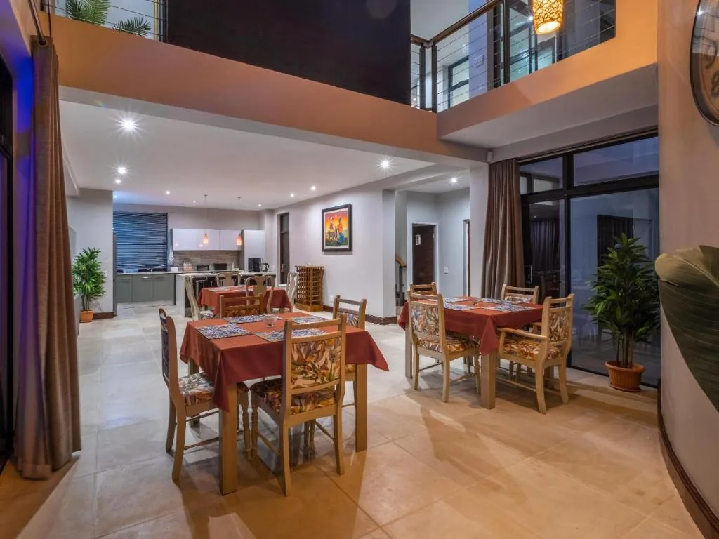 Open-plan dining area with wooden chairs and red tablecloth, kitchen visible beyond
