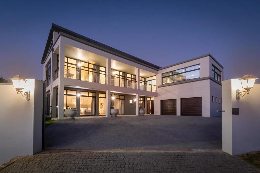 Modern two-story home with illuminated windows and paved driveway at dusk