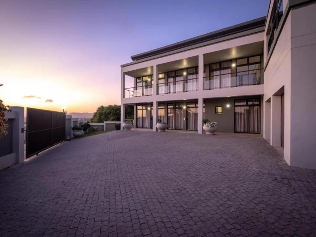 Modern two-story white home with illuminated deck at twilight, paved driveway