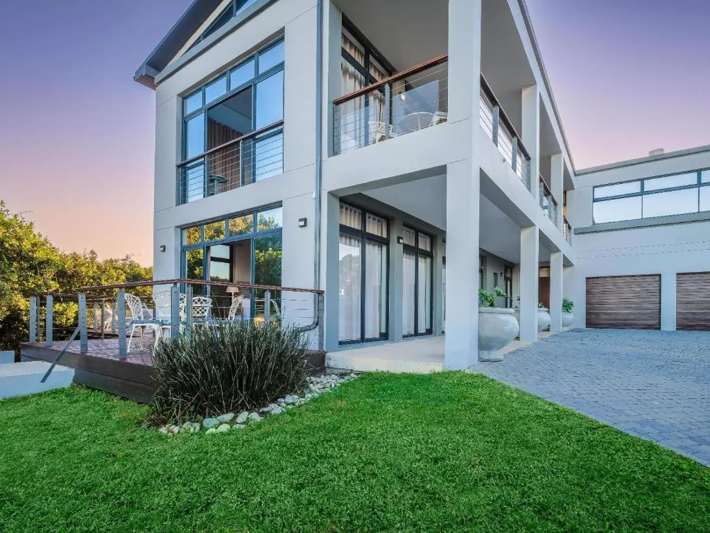 Modern white house exterior with manicured lawn and deck at dusk