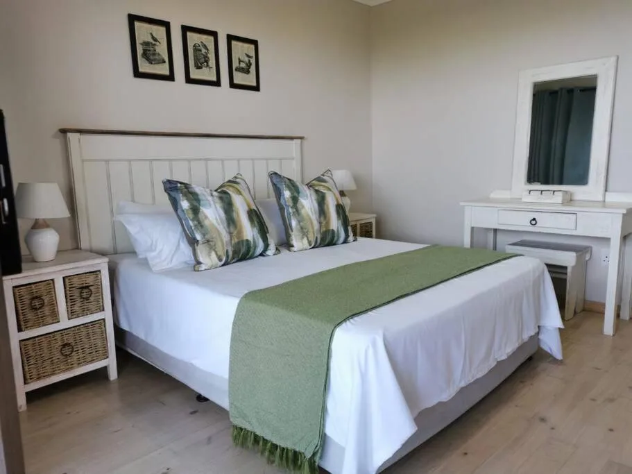 Spacious bedroom with white bed, striped pillows, green throw blanket, and vanity mirror