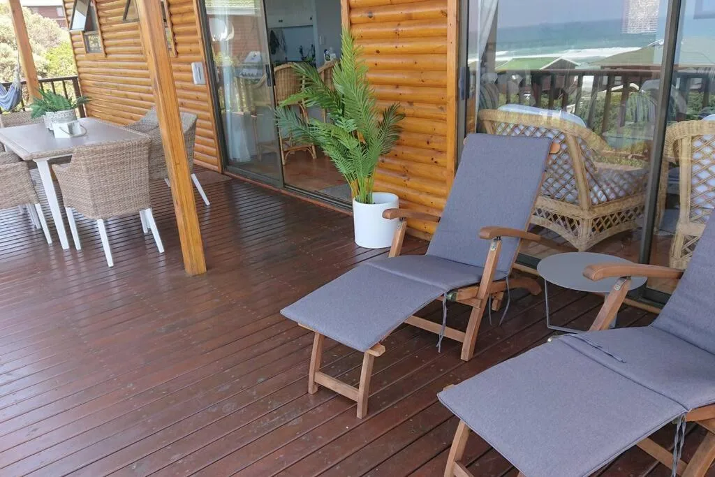Wooden deck with loungers and ocean views, adjacent to log cabin building