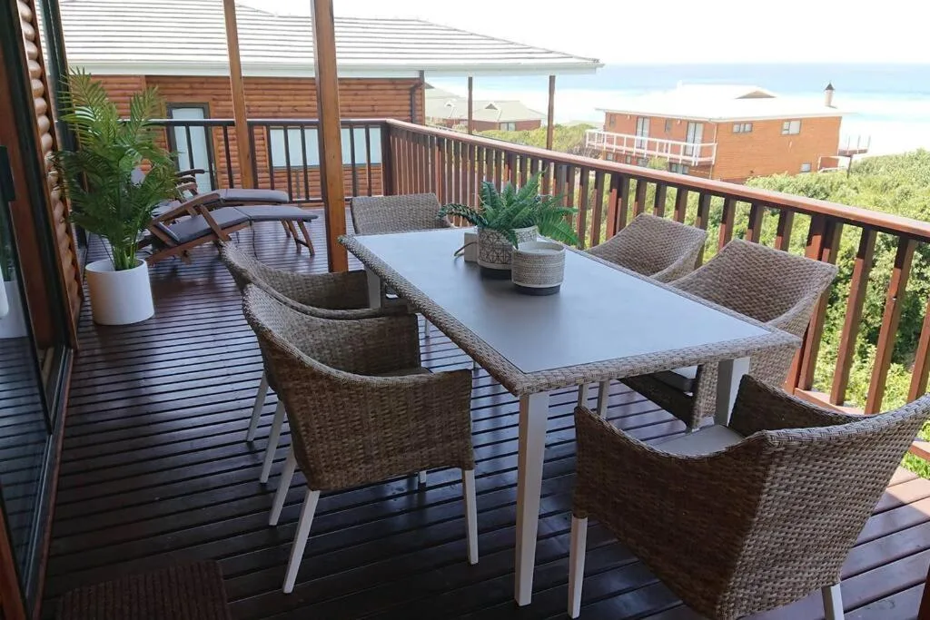 Wooden deck with wicker chairs, dining table, ocean and coastal views beyond