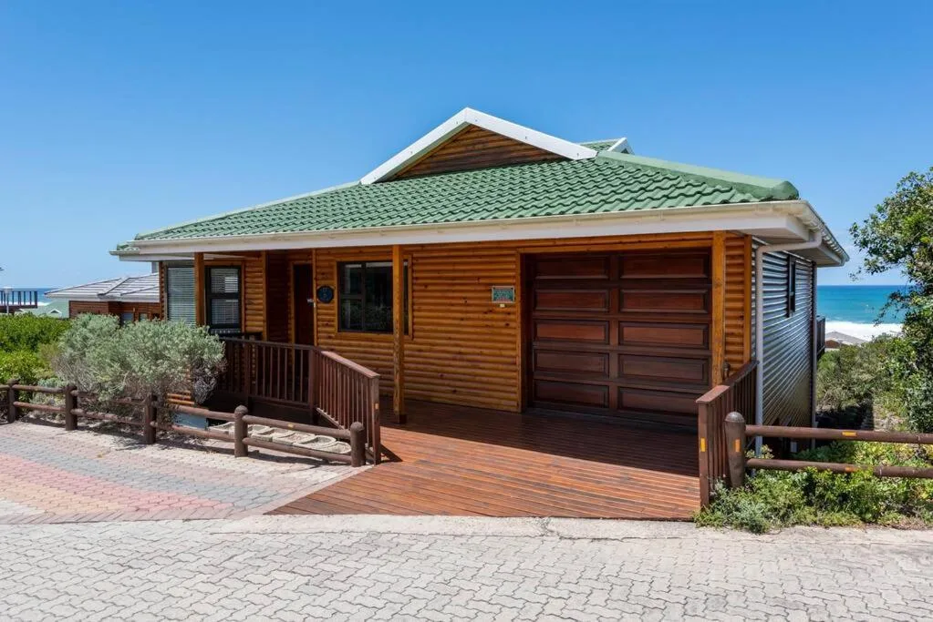 Wooden beach house with green roof and ocean view behind, clear blue sky