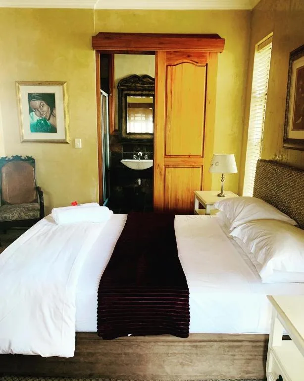 Twin beds with white linens in bright yellow bedroom with en-suite bathroom
