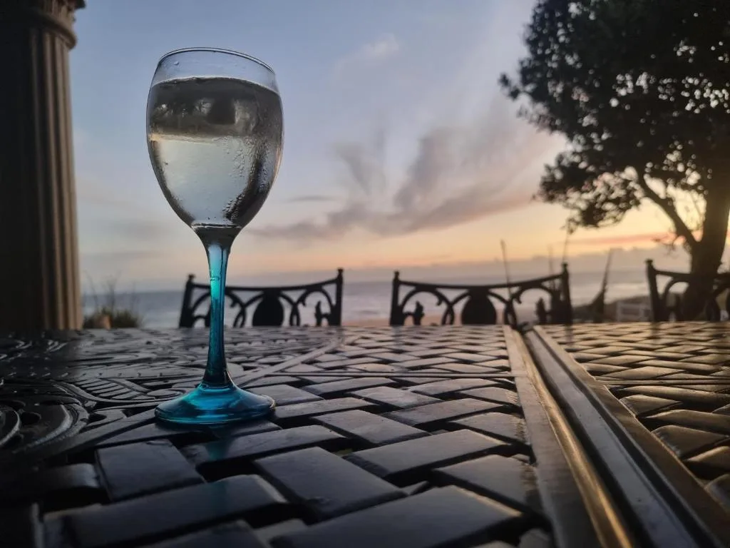 Wine glass on patterned deck with ocean sunset view and seating