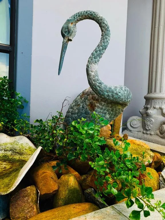 Decorative heron sculpture with green patina adorns garden landscaping