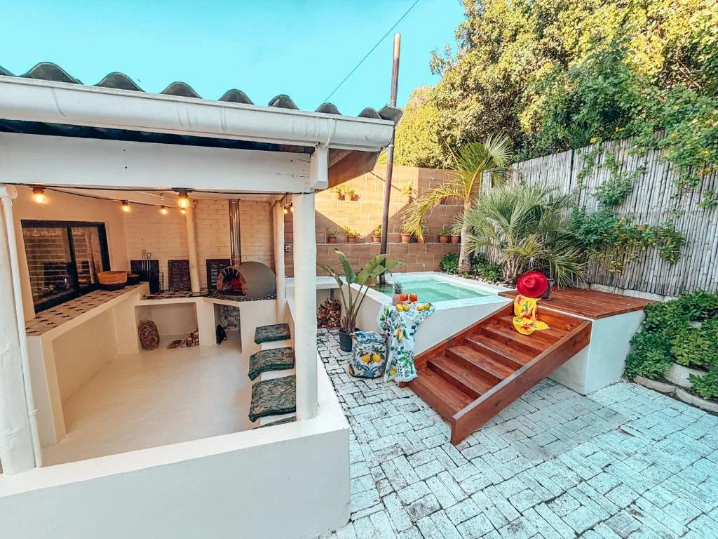 Outdoor patio area with pool, wooden deck steps, and braai covered shelter