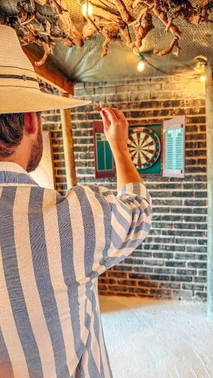 Person playing darts on covered outdoor patio with brick walls