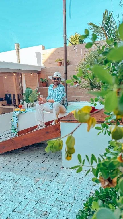 Man sitting on wooden bench in courtyard with flowering plants and pool area