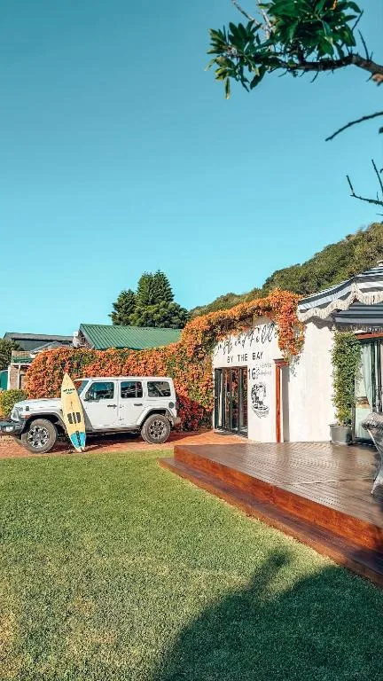 White vehicle parked at charming white cottage with ivy-covered walls and deck
