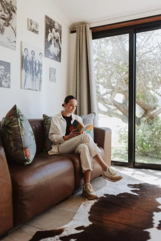 Woman reading on brown leather armchair by large window with garden views