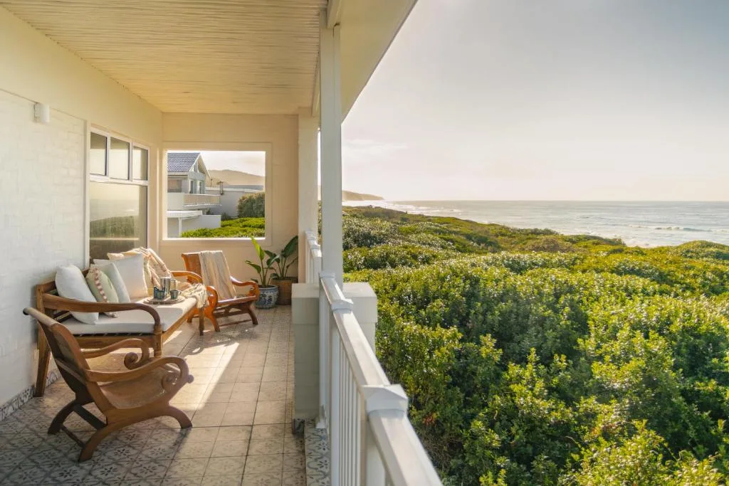 Covered patio with wooden chairs overlooking ocean and coastal vegetation