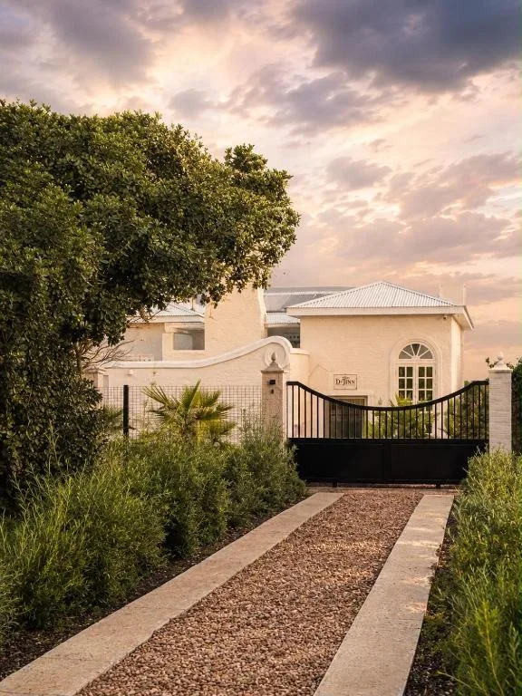 Cream-colored house with black gate entrance and manicured gardens at dusk