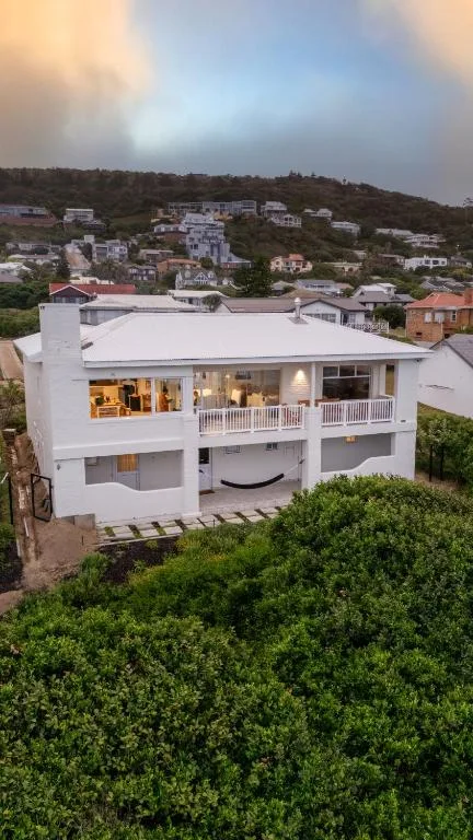 Modern white multi-level home with deck overlooking coastal hills at dusk