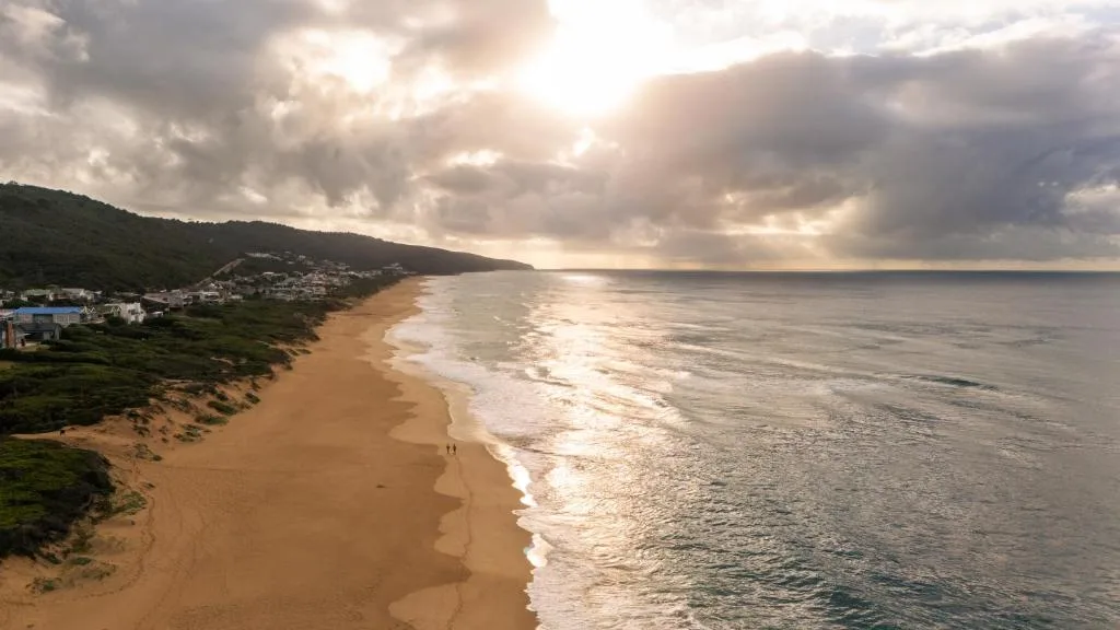 Scenic coastal view of sandy beach, ocean waves, and green hillside properties