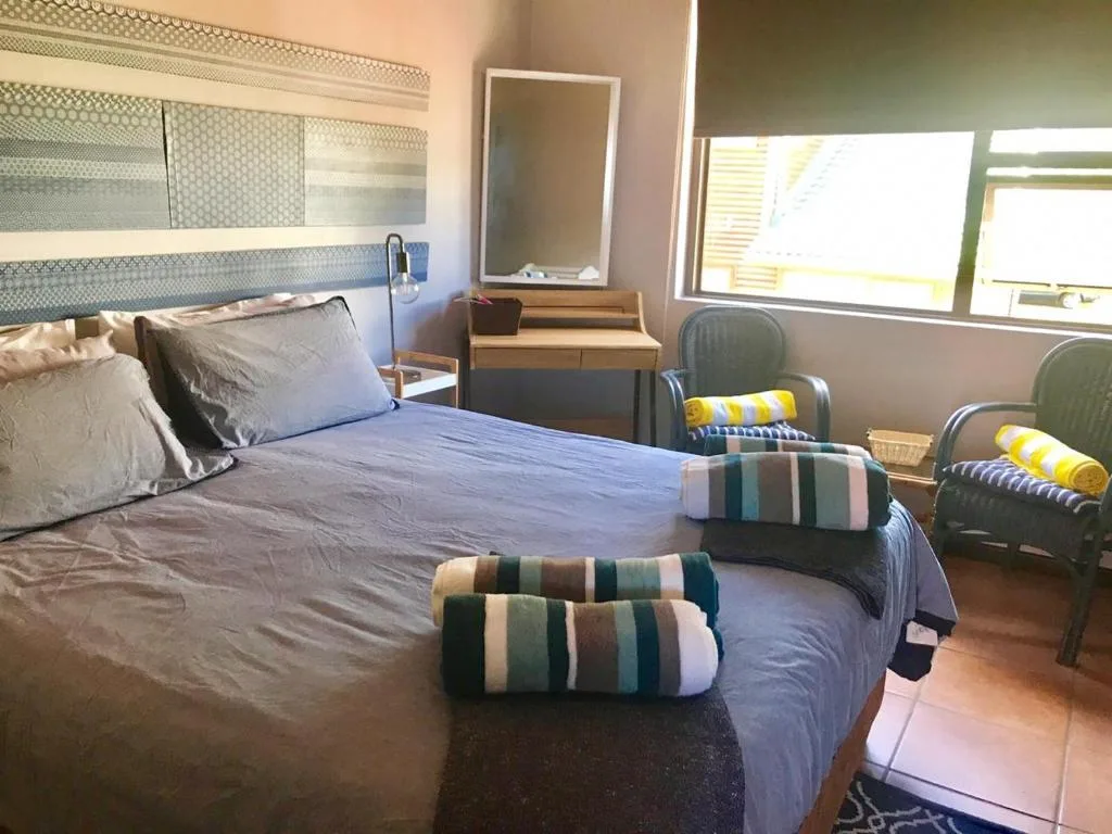 Bright bedroom with double bed, striped blankets, wooden dresser, and armchairs