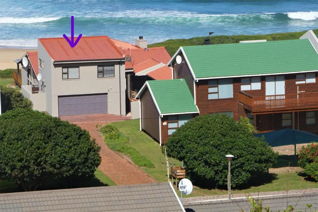 Beachfront property with cream and terracotta house, green lawn, ocean view behind