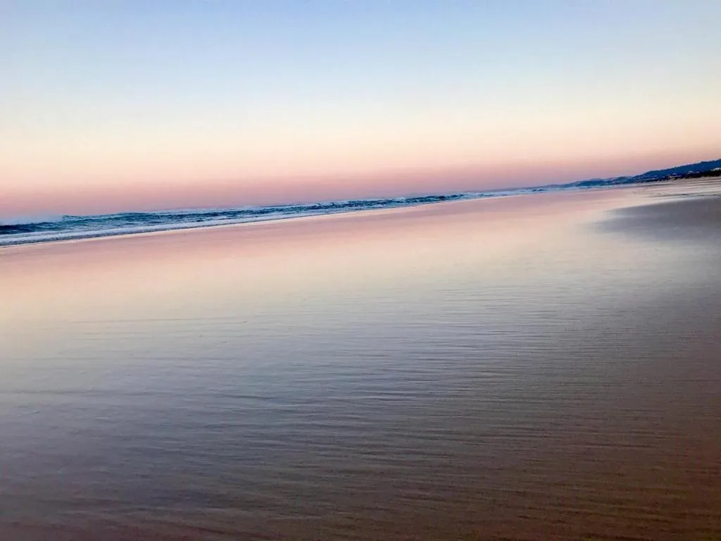 Serene beach at sunset with calm waters and distant mountains