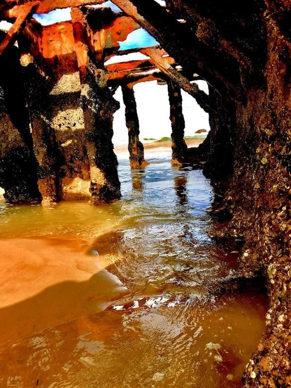 Scenic coastal view through rusty pier pillars to ocean and beach