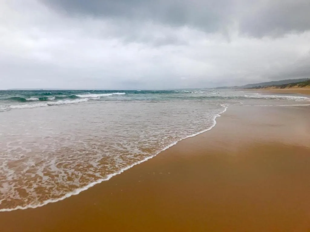 Sandy beach with rolling waves and coastal cliffs under cloudy skies