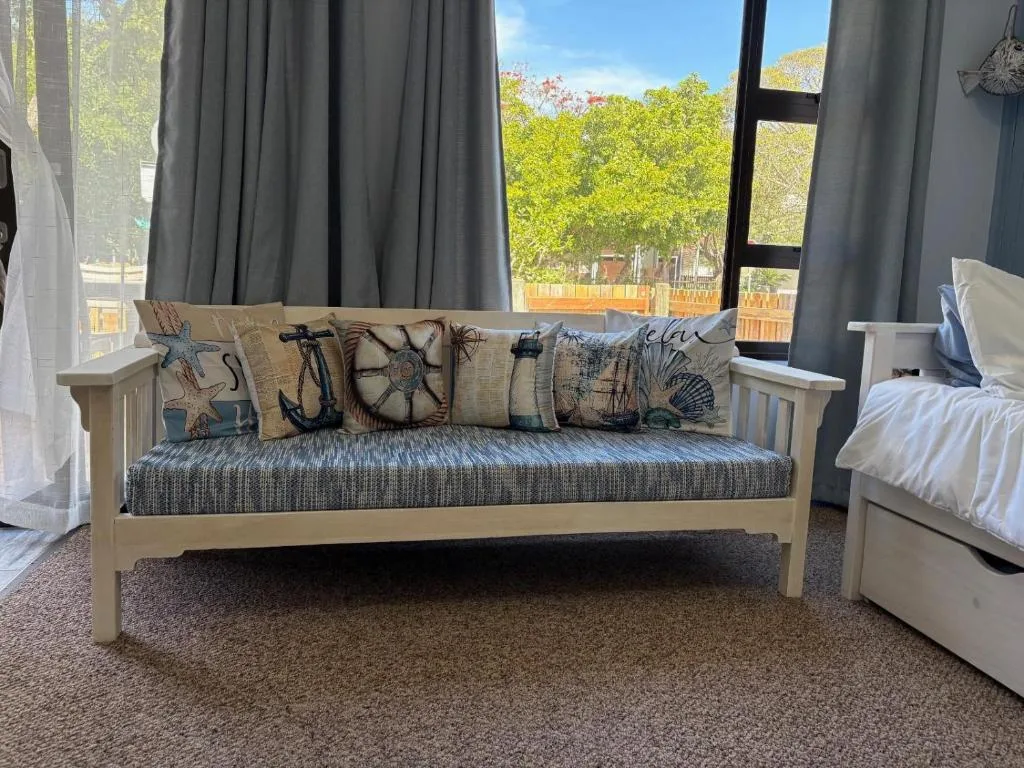 Bedroom with wooden daybed, nautical cushions, and garden views through windows