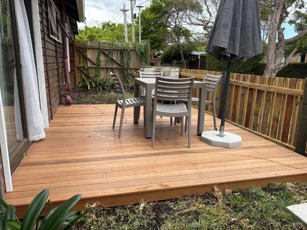 Wooden deck with dining table, chairs, and umbrella overlooking garden