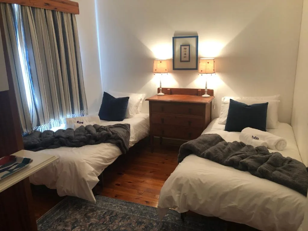 Twin bedroom with white linens, wooden dresser, and warm lighting