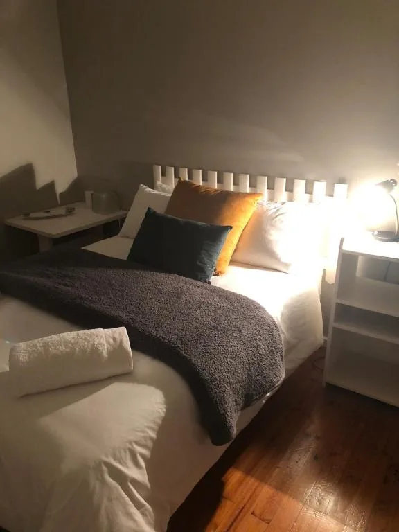 Bright bedroom with white headboard, dark bedding, and warm lighting throughout