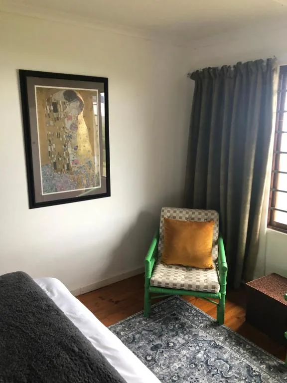 Bright bedroom corner with green chair, framed artwork, and draped curtains