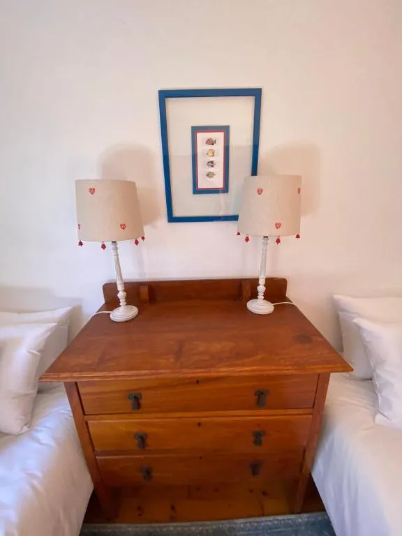 Wooden dresser with lamps between two white-dressed beds in bedroom