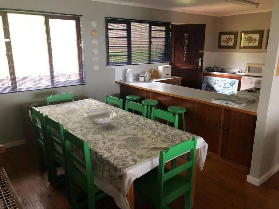 Spacious dining area with green chairs and wooden kitchen counter beyond