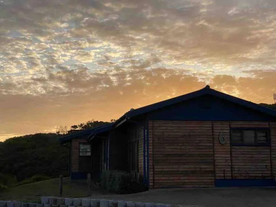 Wooden cottage with blue trim at golden sunset, surrounded by hills