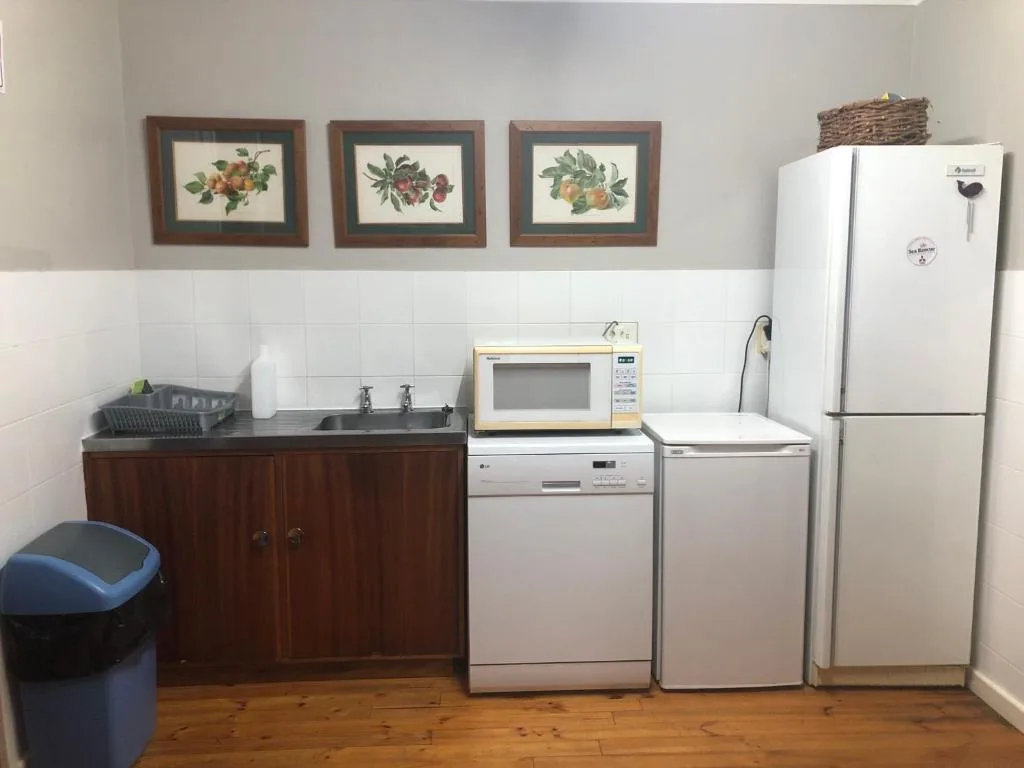 Compact kitchen with dark wooden cabinetry, white appliances, and framed botanical prints