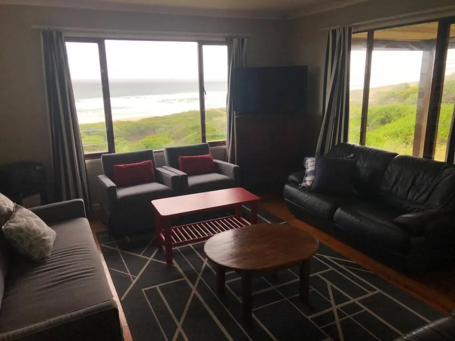 Spacious lounge with black leather sofa and armchairs overlooking lagoon
